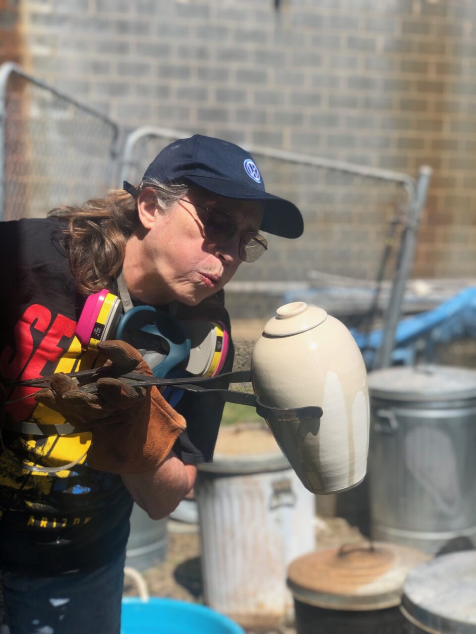Judi Harwood holding hot raku pot with tongs, blowing on crackle glaze Judi Harwood holding hot raku pot with tongs, blowing on crackle glaze