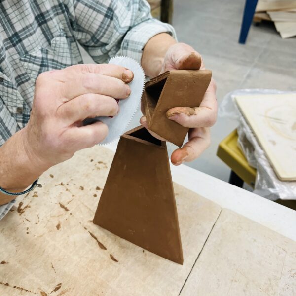 Close up of hands assembling slab built triangle vase, scoring with metal rib