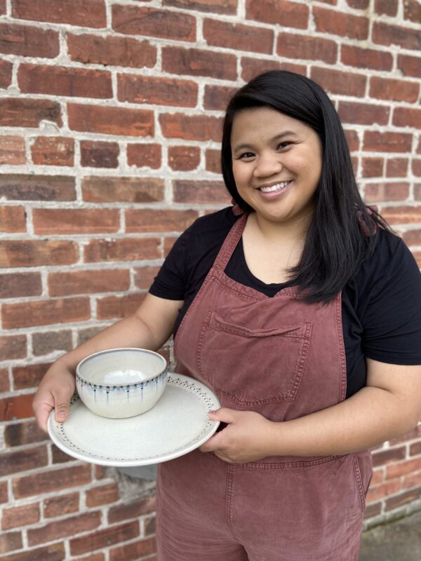Katie Meili Messersmith holding finished pots, dinner plate and cereal bowl, dot pots
