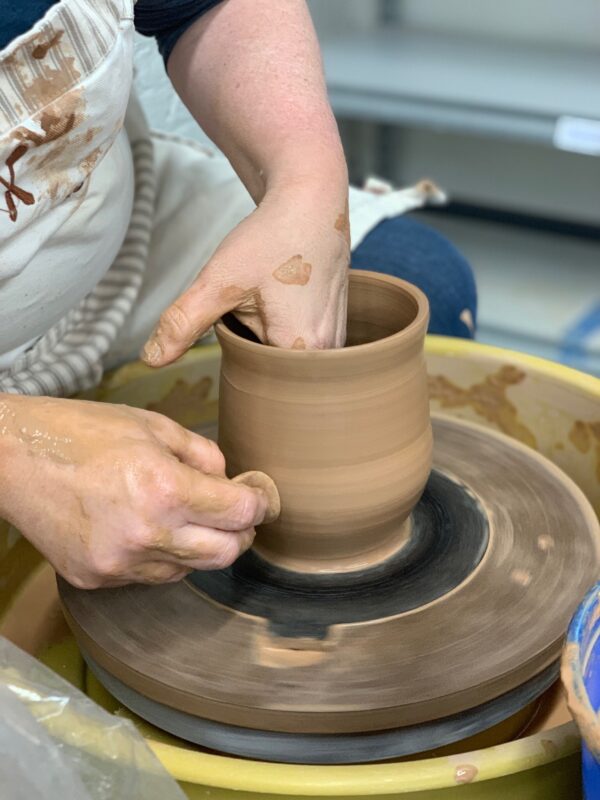 Close up student hands throwing on potters wheel, red clay