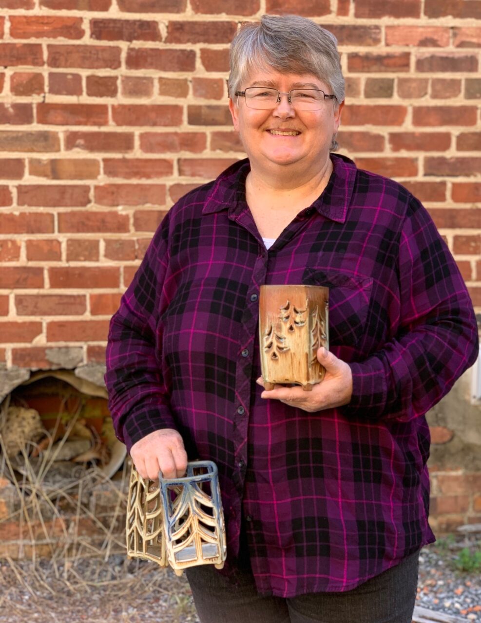 Julia Mann standing, smiling while holding her finished pots, pierced lanterns Julia Mann standing, smiling while holding her finished pots, pierced lanterns