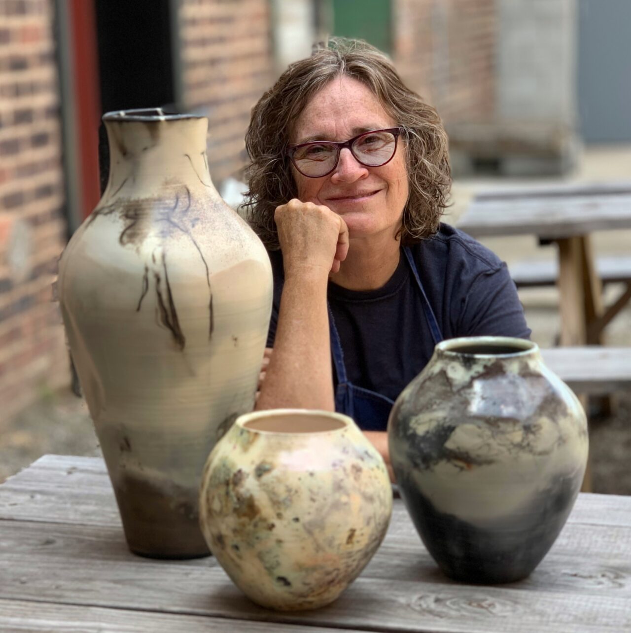 Judi Harwood sitting with a grouping of her finished pots, sagger pots Judi Harwood sitting with a grouping of her finished pots, sagger pots