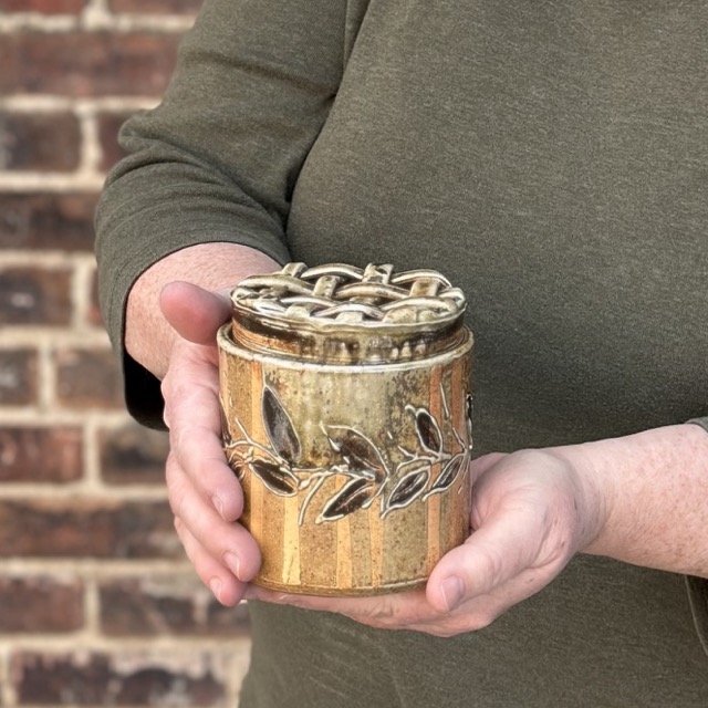 Karen Dubois holding finished hand built pot, vase with woven lid, wood soda kazie fired Karen Dubois holding finished hand built pot, vase with woven lid, wood soda kazie fired
