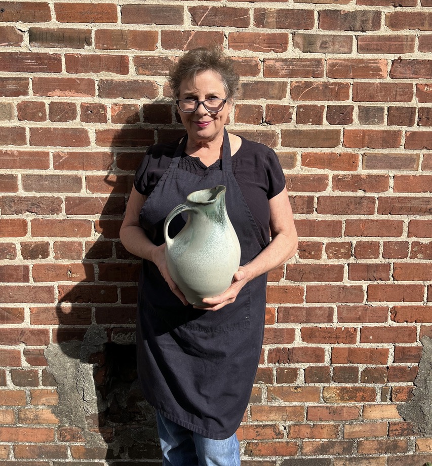 Sarah Wells Rolland holding finished pot, pouring vessel, pitcher, stoney blue glaze Sarah Wells Rolland holding finished pot, pouring vessel, pitcher, stoney blue glaze